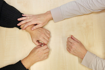Zwei Personen von oben an einem Tisch: Fokus auf Hände, die einander berühren