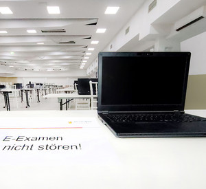 Laptop im Prüfungssaal mit einem Schild mit der Aufschrift " E-Examen - Bitte nicht stören!"