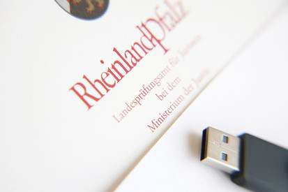 Zeugnis mit der Aufschrift „Rheinland-Pfalz – Landesprüfungsamt für Juristen bei dem Ministerium der Justiz“ und ein schwarzer USB-Stick