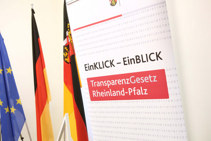 Roll-Up mit der Aufschrift „EinKLICK-EinBLICK TransparenzGesetz Rheinland-Pfalz und drei Fahnen (Europa, Deutschland und Rheinland-Pfalz)