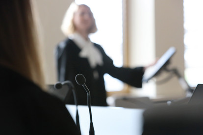 Staatsanwältin stehend während des Verlesens der Anklageschrift von einem Bildschirm